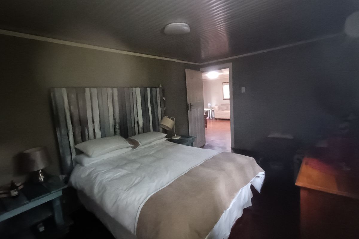 A bedroom featuring a neutral color palette, wood-look flooring, and a doorway leading to an adjacent living space.