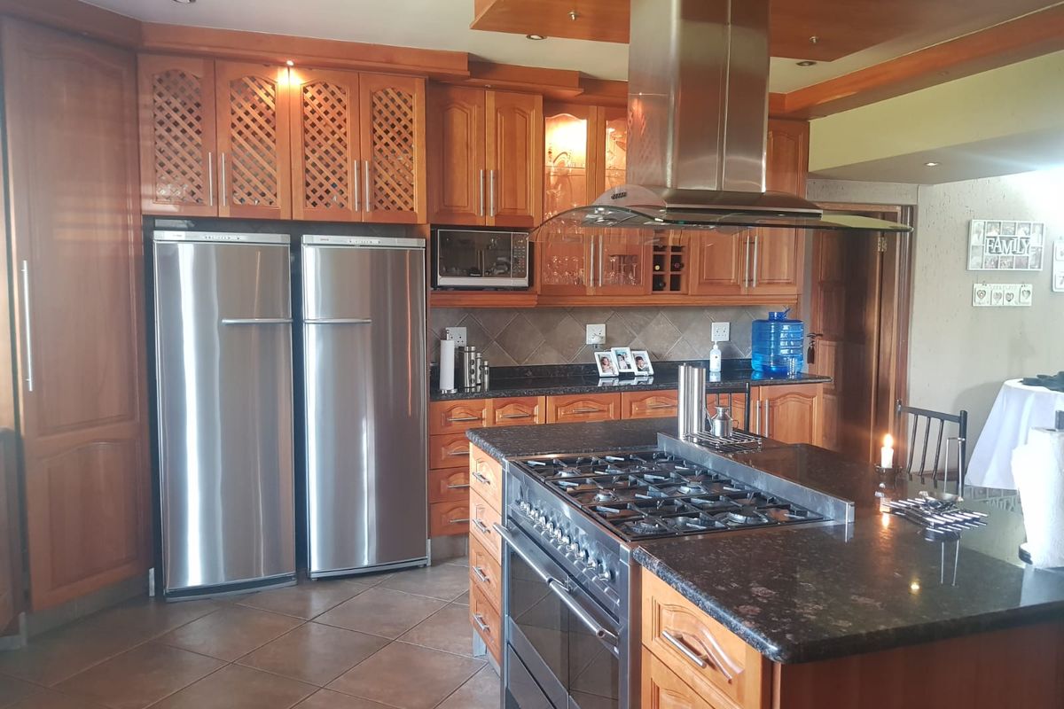 Spacious kitchen featuring solid wood cabinetry, granite countertops, a central island with a gas hob, and a stainless steel extractor fan.
