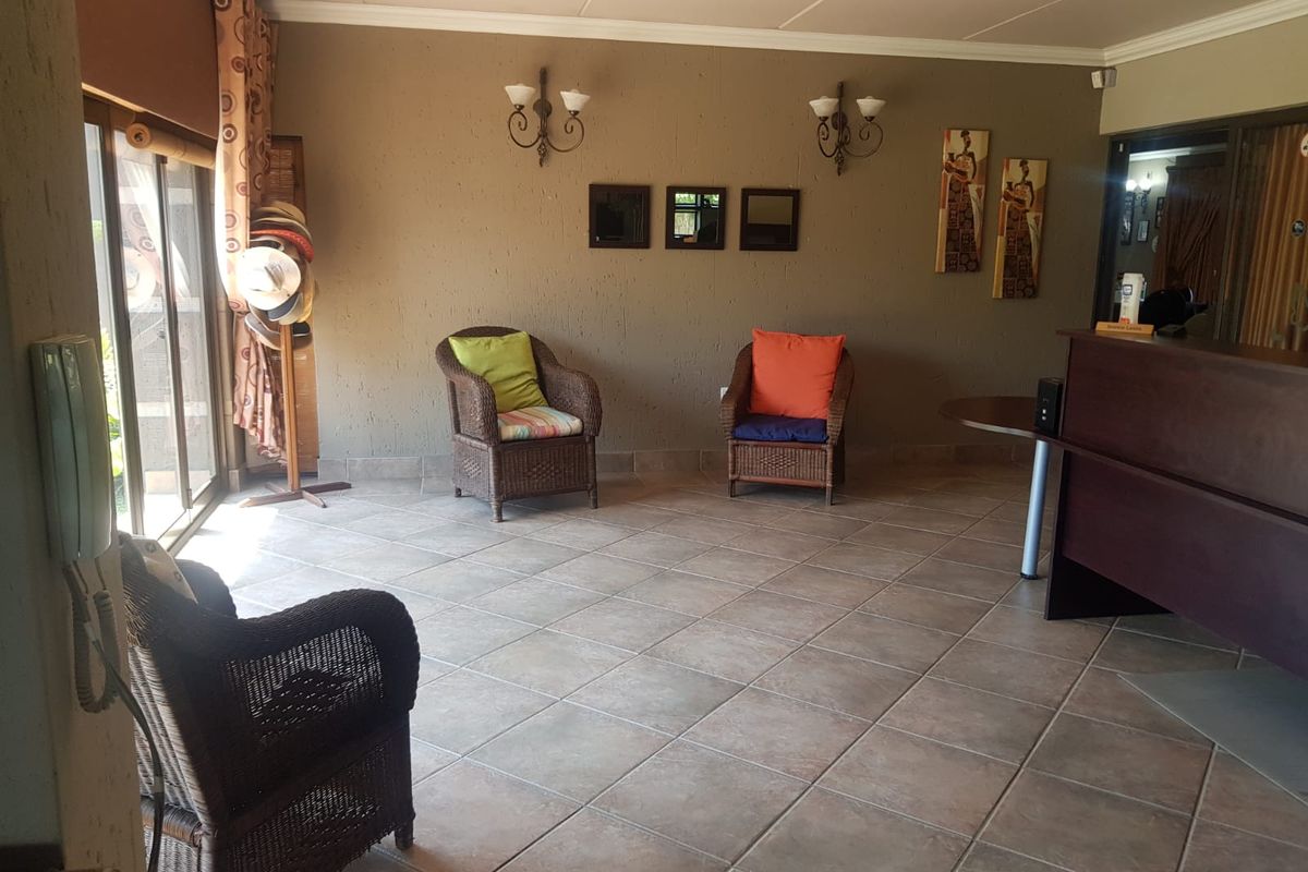 A spacious reception or lounge area featuring tiled flooring, wall-mounted light fixtures, and large sliding glass doors providing access to the exterior.