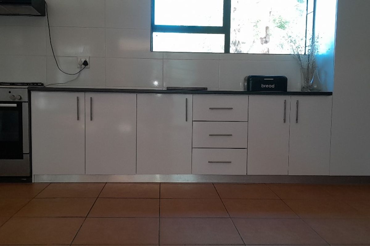 A clean, functional kitchen featuring white cabinetry, stainless steel oven, extractor fan, tiled backsplash, and durable floor tiles.