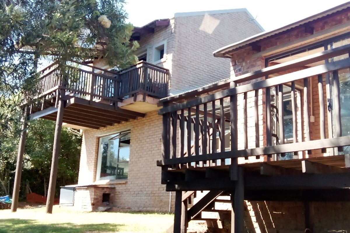 Rear view of a multi-level farm house featuring elevated timber decks, exposed brick facade, and large sliding glass doors overlooking the garden.