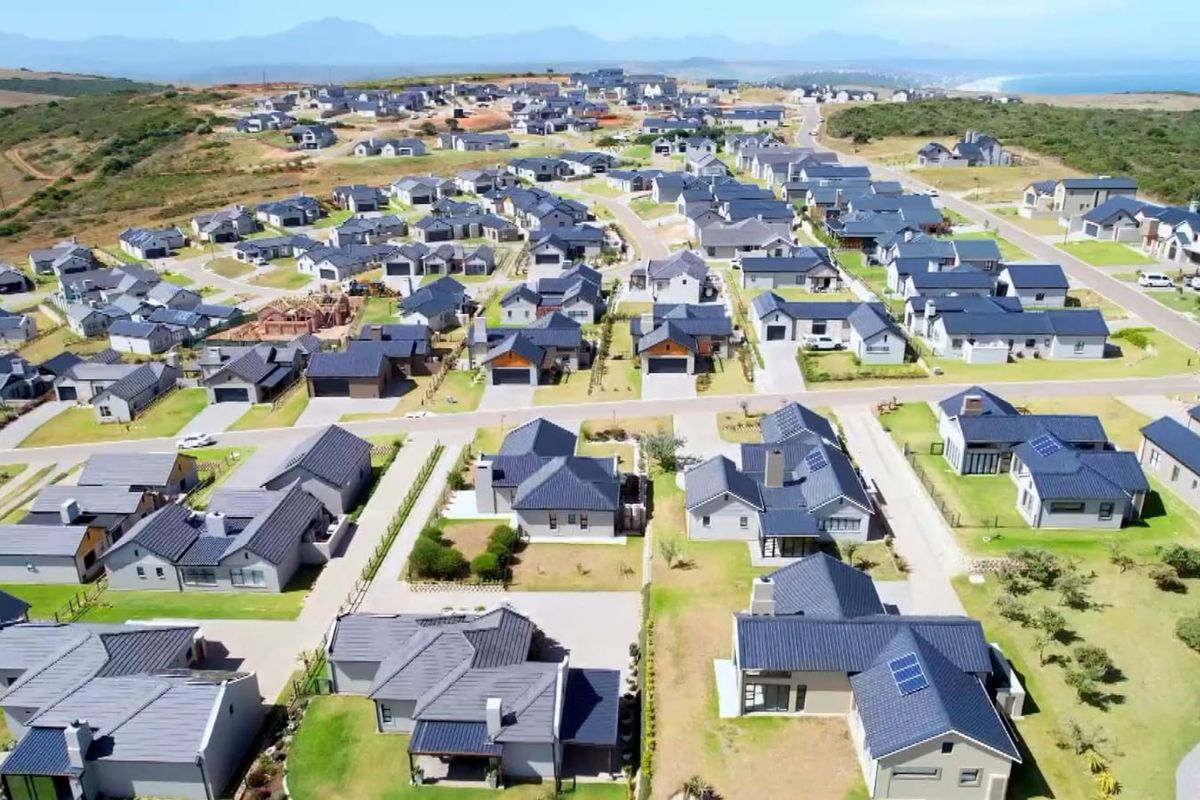 An elevated aerial view of a modern residential estate featuring numerous detached houses with dark tiled roofs and landscaped surroundings.
