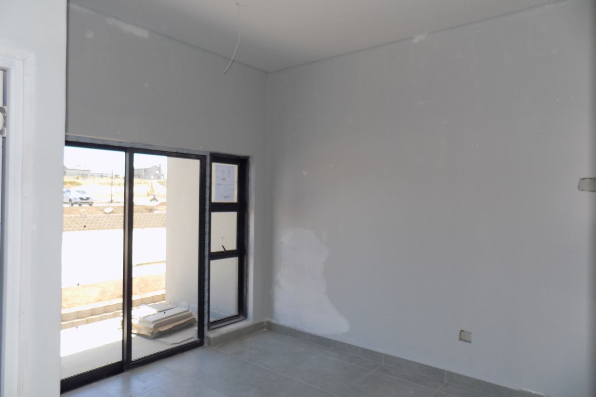 An empty, unfinished room featuring large sliding glass doors leading to an outdoor area, tiled flooring, and neutral wall finishes.
