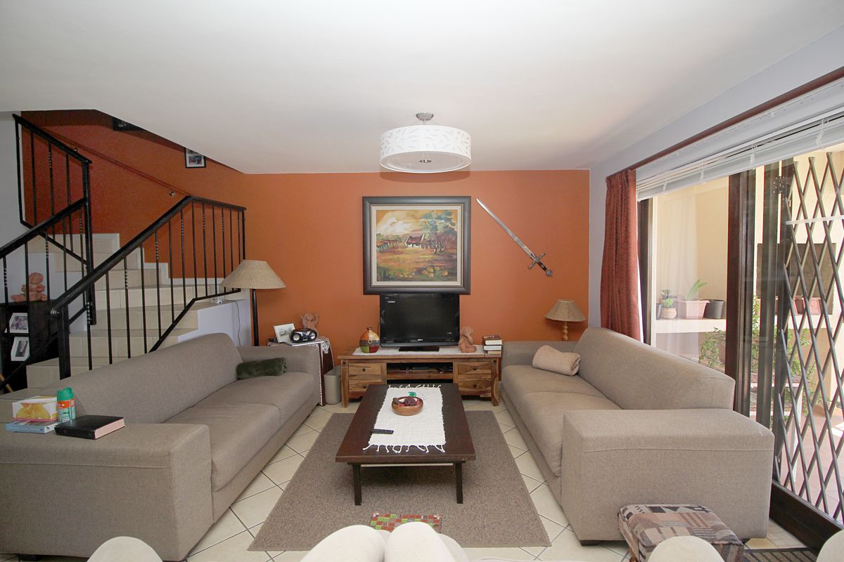 Spacious living room featuring tiled flooring, a staircase with a metal balustrade, and sliding glass doors leading to an outdoor area.