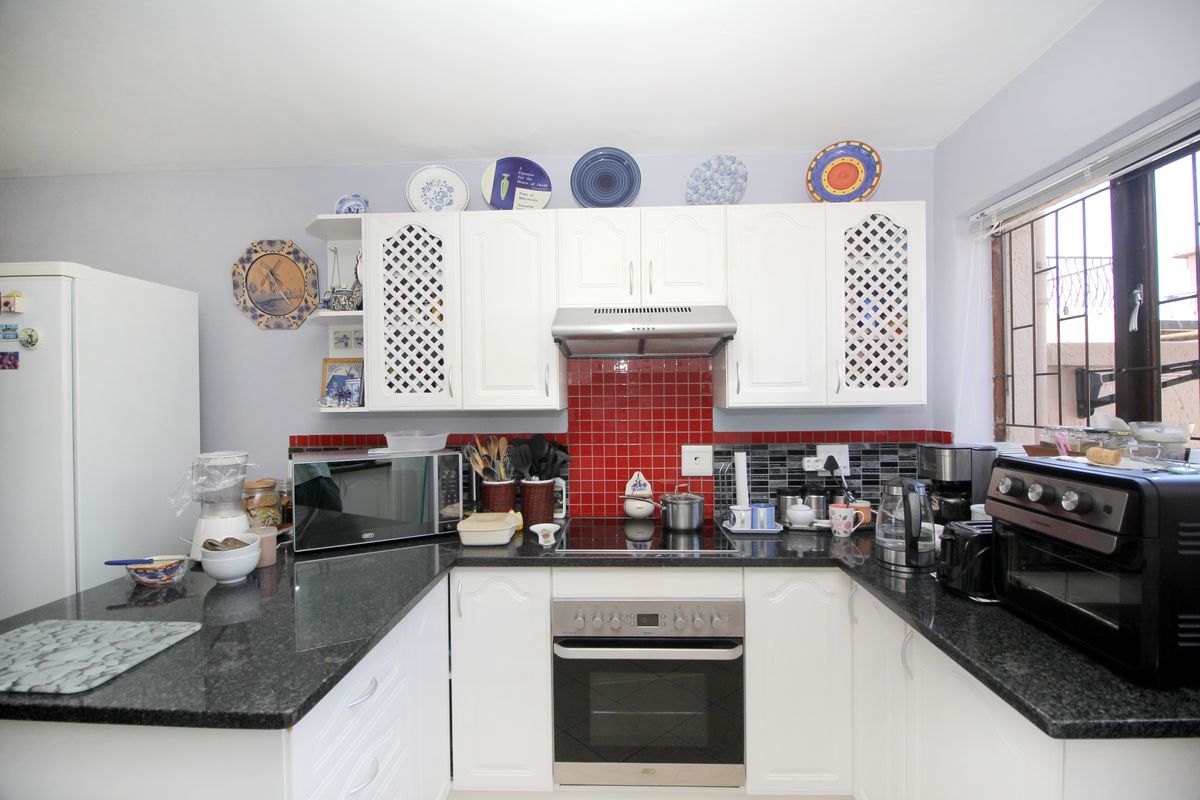 A functional kitchen featuring white cabinetry, dark granite countertops, a red tiled splashback, and integrated cooking appliances.