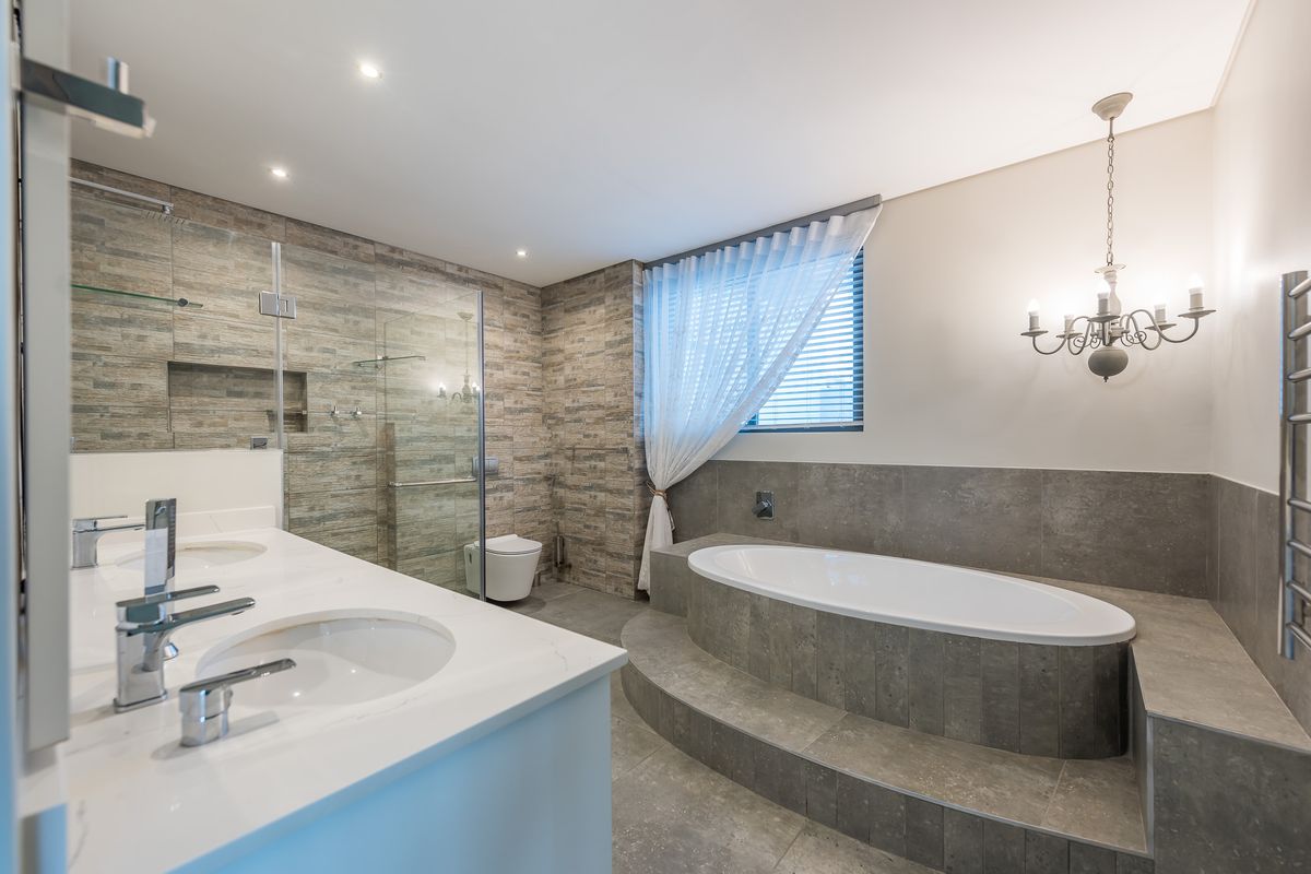 Modern bathroom featuring a raised oval soaking tub, dual vanity with stone countertop, glass-enclosed walk-in shower, and elegant stone wall tiling.
