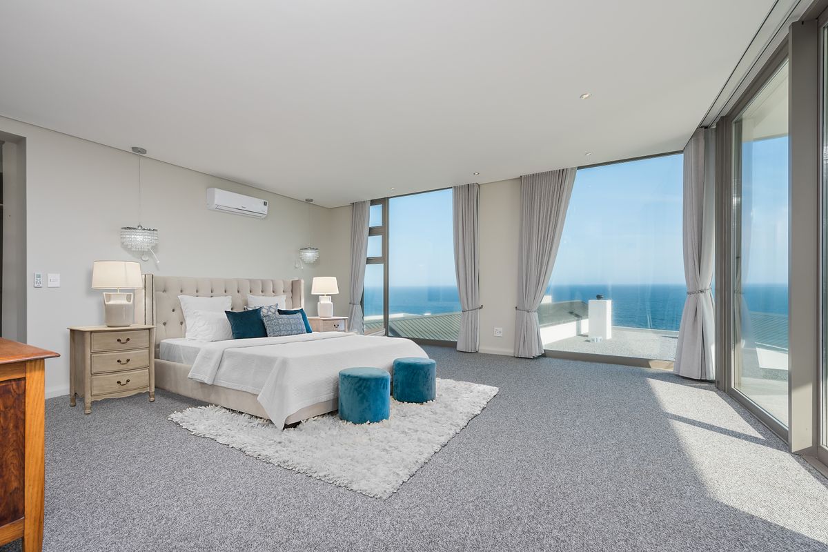 Spacious bedroom featuring floor-to-ceiling glass sliding doors with expansive ocean views, wall-mounted air conditioning unit, and neutral carpeting.