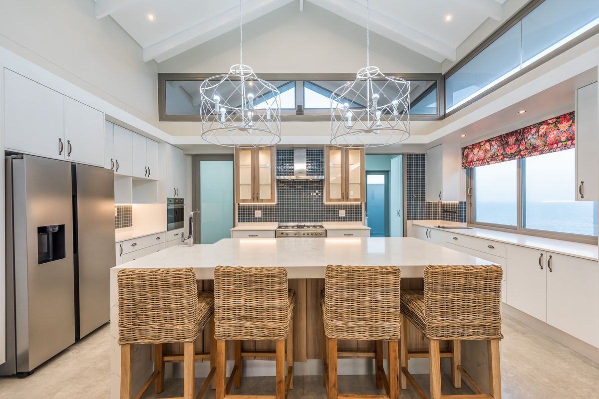 Modern kitchen featuring a large central island, stone countertops, built-in stainless steel appliances, and high vaulted ceilings with clerestory windows.