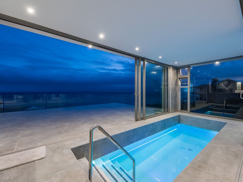 Indoor plunge pool featuring modern tiled finishes, recessed lighting, and large sliding glass doors opening to an expansive outdoor terrace with ocean views.