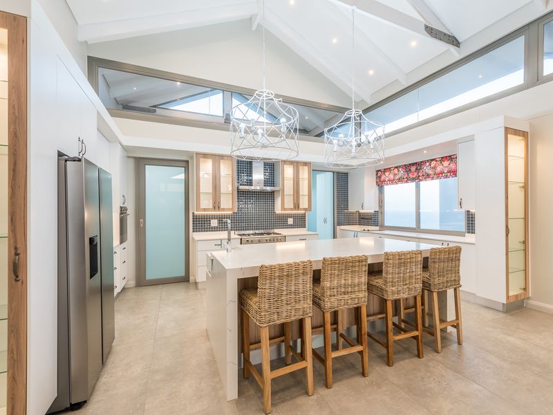 Modern open-plan kitchen featuring a large central island, stone countertops, built-in stainless steel appliances, and high vaulted ceilings with clerestory windows.