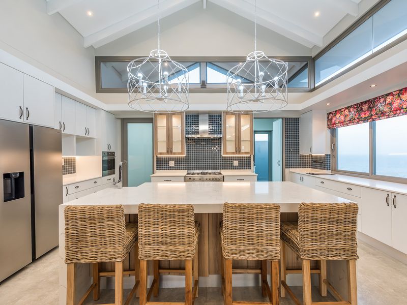 Modern kitchen featuring a large central island, stone countertops, built-in stainless steel appliances, and high vaulted ceilings with clerestory windows.