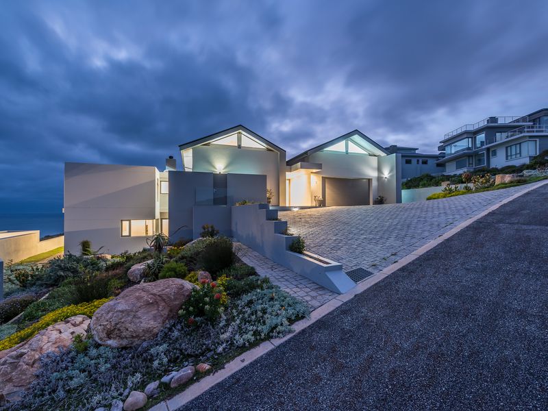 Modern architectural residence featuring a paved driveway, integrated garage, and landscaped terraced garden with coastal views at dusk.
