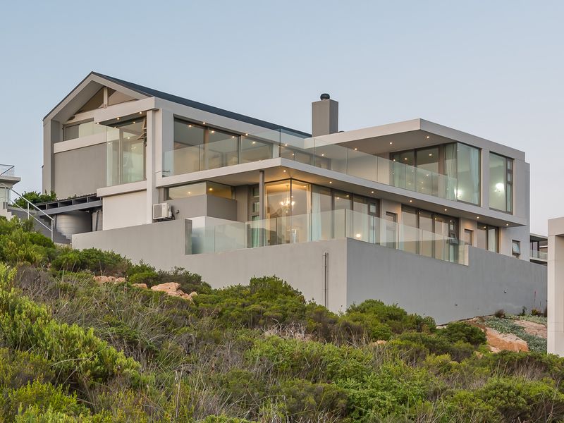 Modern multi-level architectural home featuring expansive glass facades, sleek balconies with glass balustrades, and a contemporary pitched roof design.