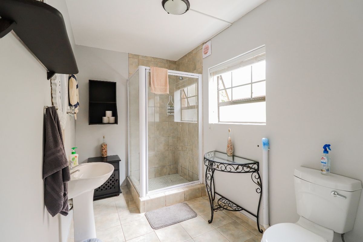 A functional bathroom featuring a corner shower enclosure, pedestal basin, and toilet with tiled flooring and natural light from a side window.