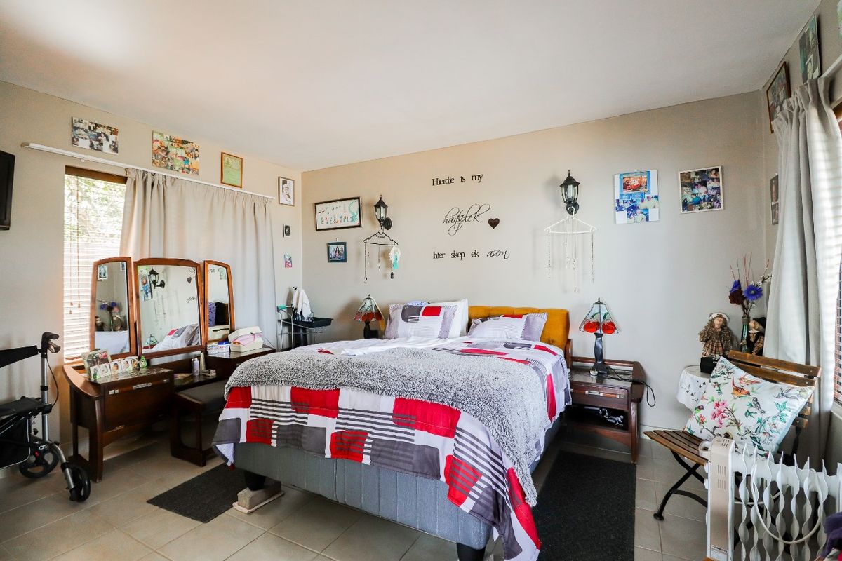 A functional bedroom featuring tiled flooring, wall-mounted light fixtures, and large windows with curtain tracks.
