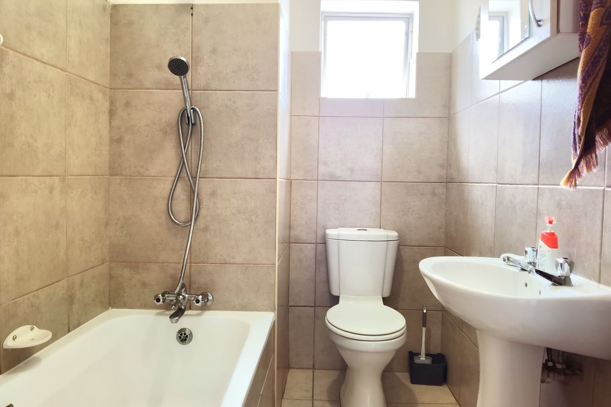 A functional bathroom featuring a bathtub with shower attachment, pedestal basin, and toilet, finished with neutral wall and floor tiles.