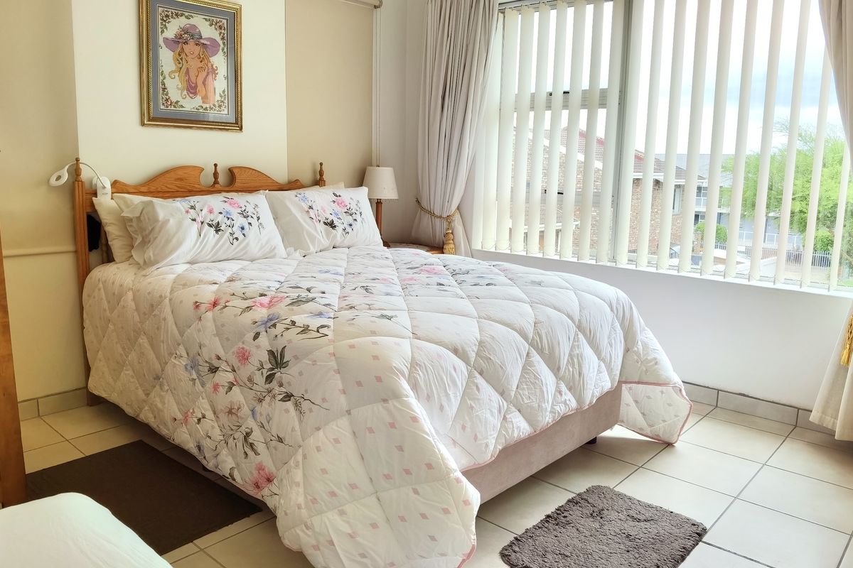 A well-lit bedroom featuring tiled flooring and large windows with vertical blinds, offering a functional and comfortable living space.