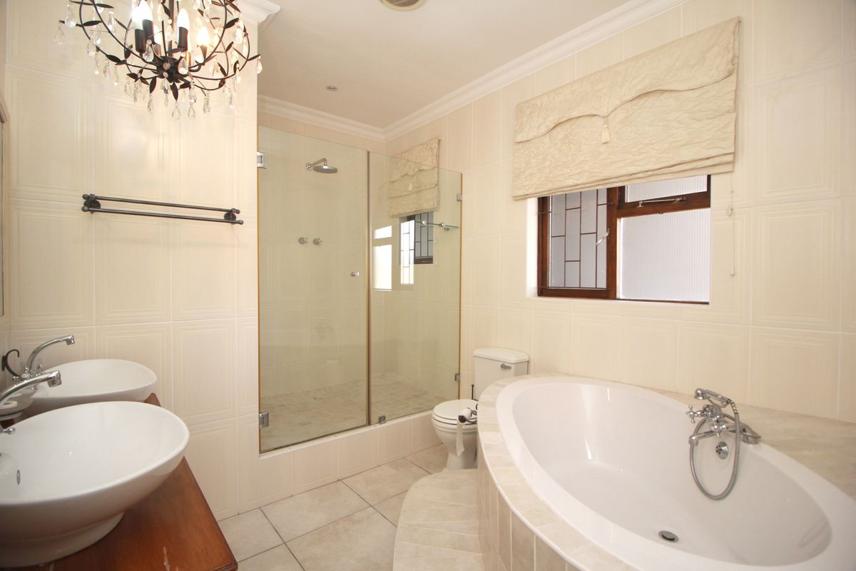 A well-appointed bathroom featuring a glass-enclosed shower, a built-in bathtub, and dual vessel sinks on a wooden vanity.