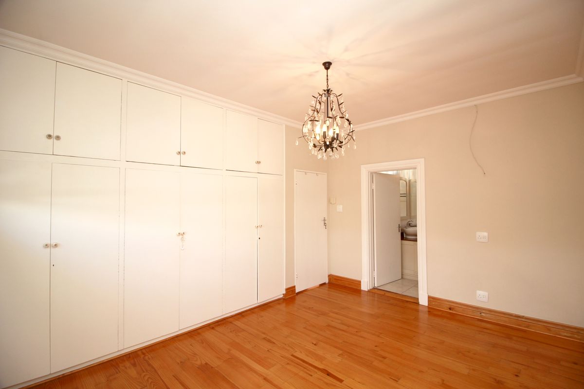 A bedroom featuring extensive built-in floor-to-ceiling cabinetry, polished wooden flooring, and an en-suite bathroom entrance.