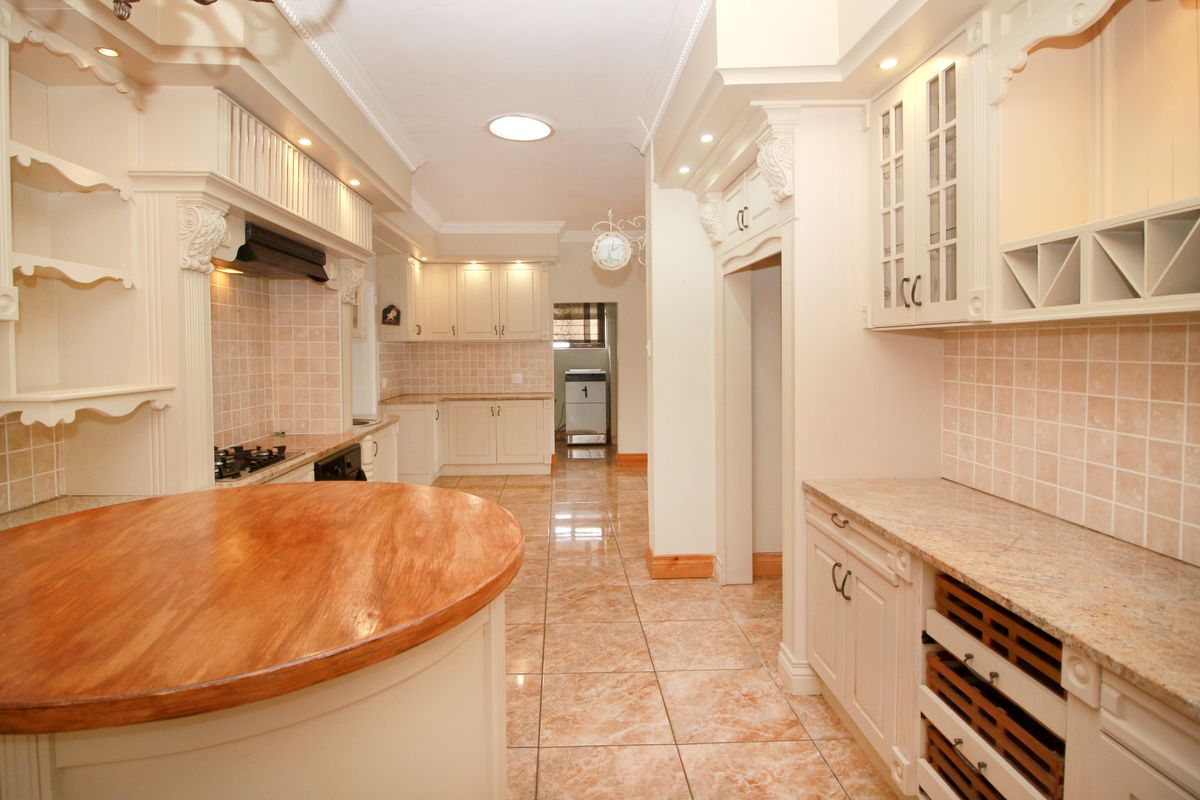 Spacious kitchen featuring classic cabinetry, granite countertops, a central wooden island, tiled flooring, and integrated storage solutions.