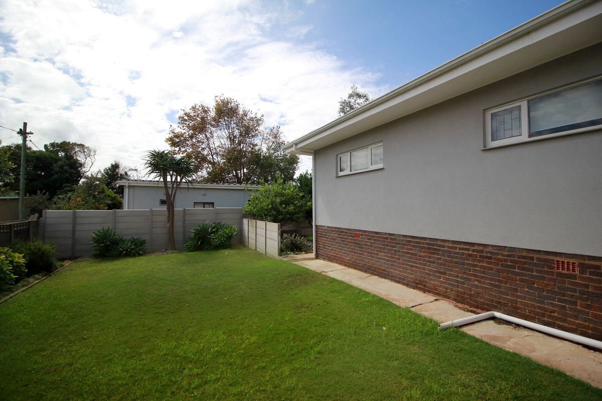 A view of the rear garden featuring a lawn area, perimeter boundary wall, and the side elevation of the house with brick and rendered finishes.