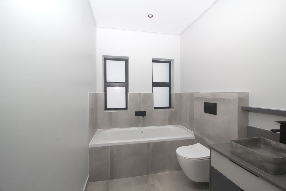 Modern bathroom featuring a built-in bathtub, wall-hung toilet with concealed cistern, and a contemporary vanity basin with neutral grey tiling.
