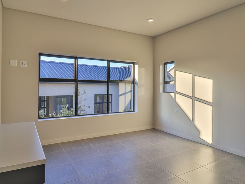 A bright, modern, and empty bedroom featuring large aluminium-framed windows, neutral tiled flooring, and a built-in desk area.