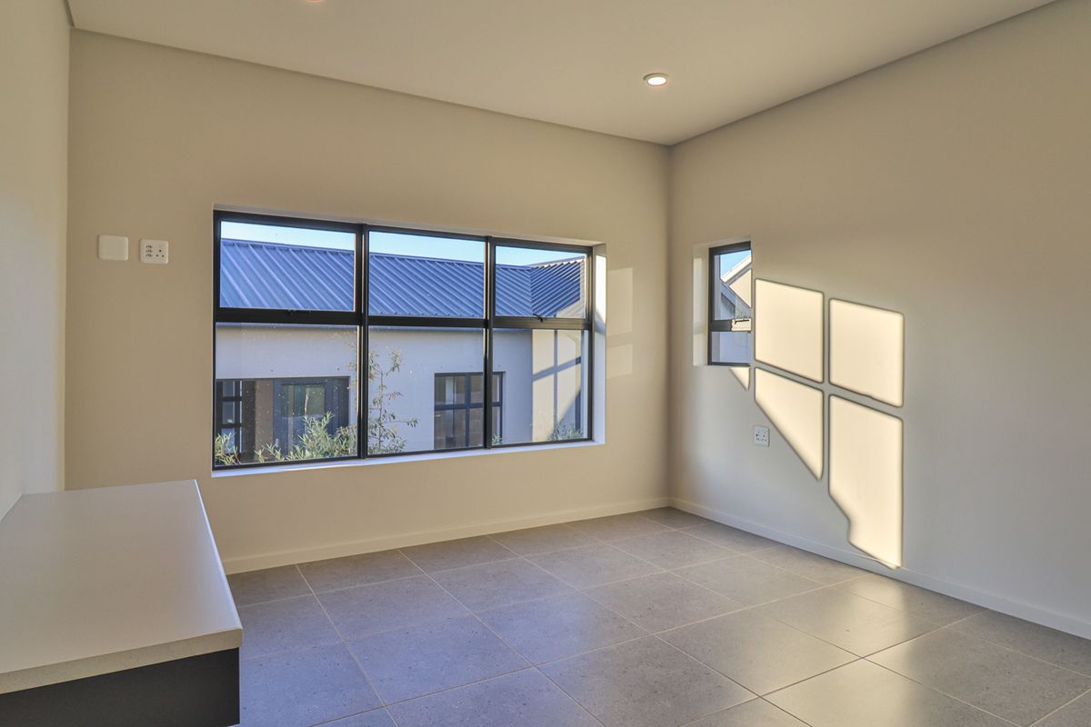 A bright, modern, and empty bedroom featuring large aluminium-framed windows, neutral tiled flooring, and a built-in desk area.