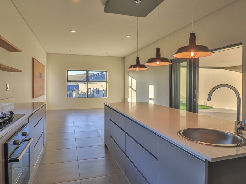 Modern kitchen featuring a central island with stone countertops, gas cooktop, built-in oven, and seamless access to the outdoor patio area.