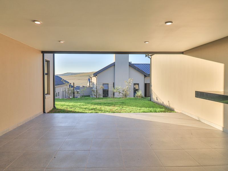 A spacious covered patio featuring tiled flooring, recessed lighting, and a built-in braai area, offering a seamless transition to the rear garden.