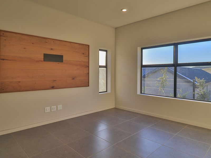 A bright, modern, and empty living room featuring large aluminium windows, neutral tiled flooring, and a decorative timber wall panel.
