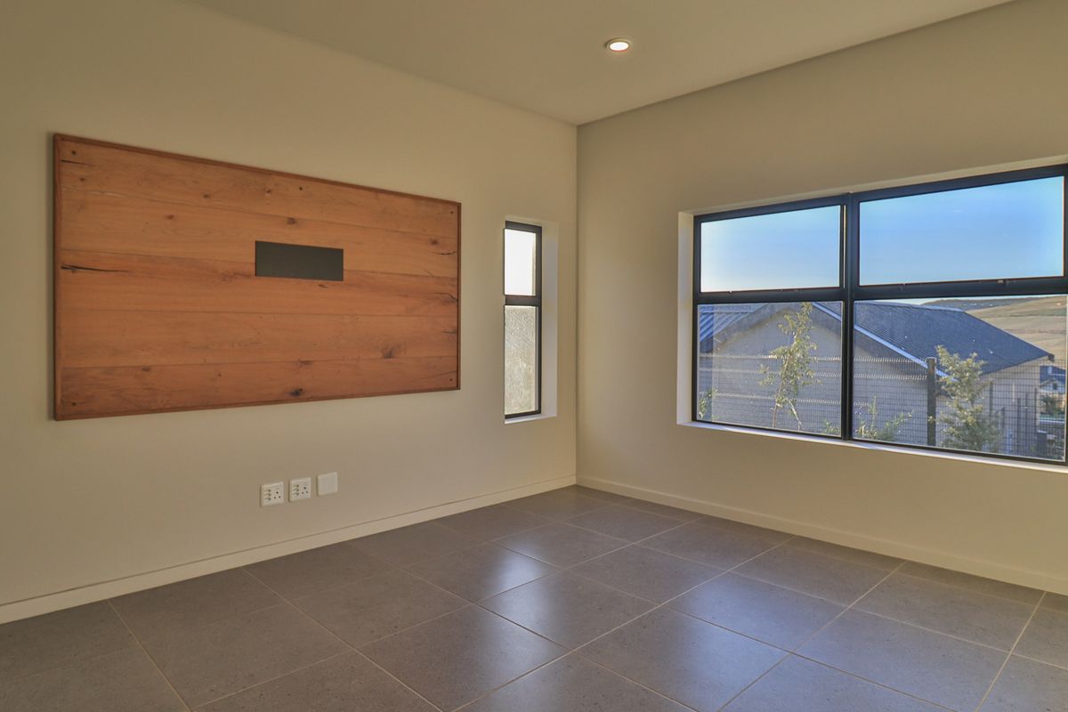 A bright, modern, and empty living room featuring large aluminium windows, neutral tiled flooring, and a decorative timber wall panel.