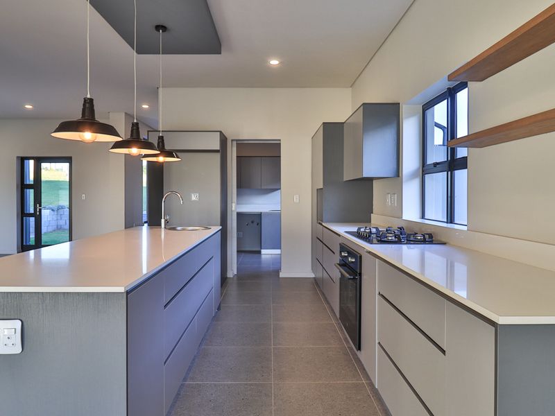 Modern kitchen featuring a central island, stone countertops, built-in oven, gas hob, and sleek cabinetry, with an adjacent scullery area.