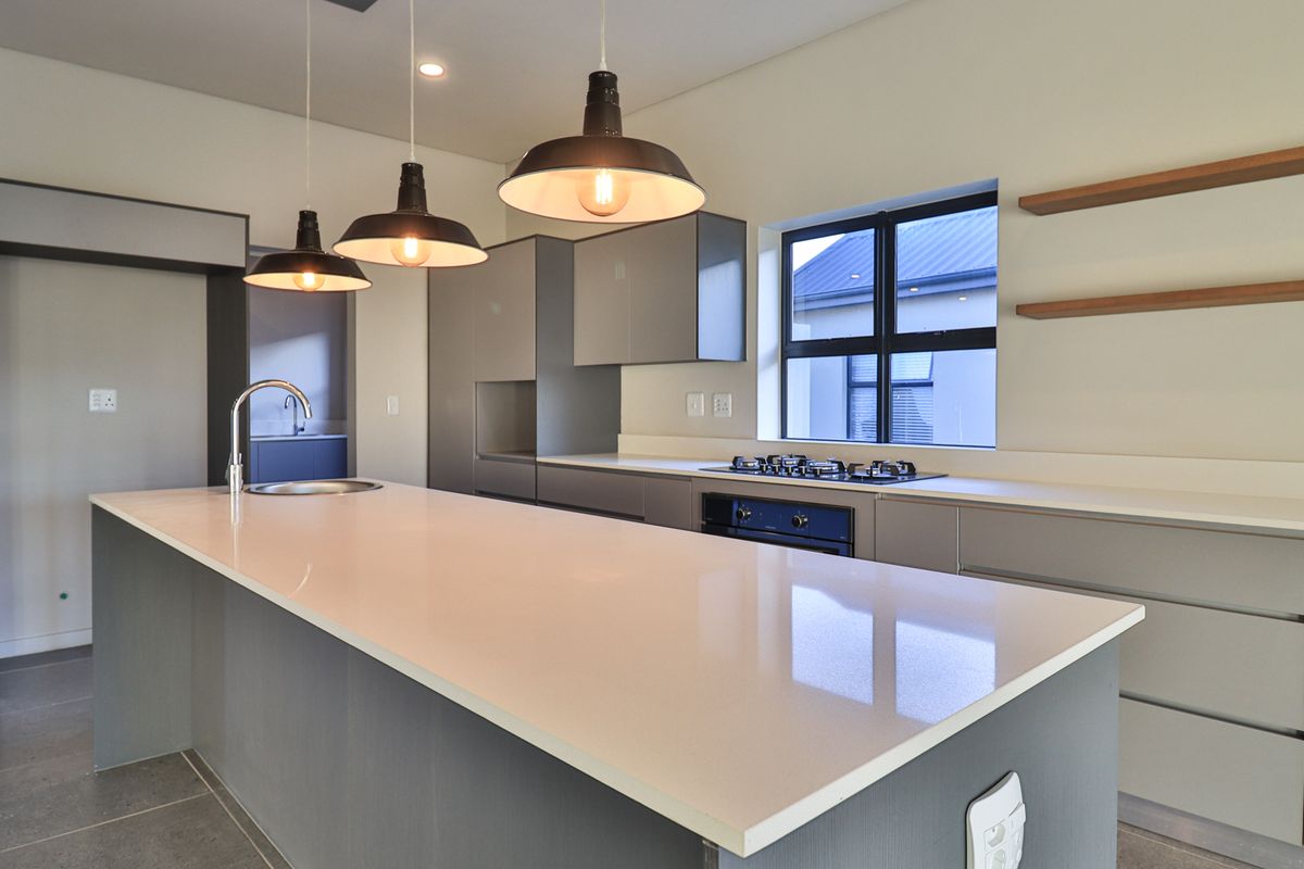 Modern kitchen featuring a large central island, quartz countertops, built-in gas hob, oven, and sleek cabinetry with contemporary pendant lighting.
