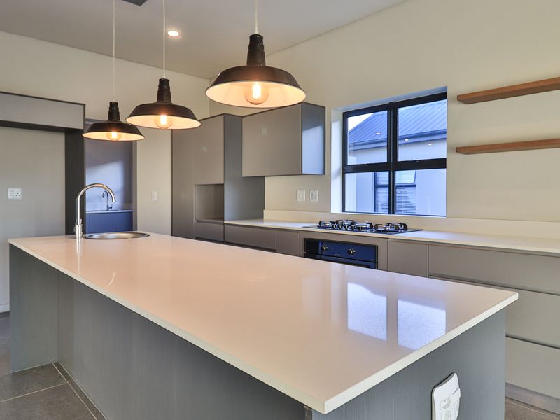 Modern kitchen featuring a large central island, quartz countertops, built-in gas hob, oven, and sleek cabinetry with contemporary pendant lighting.