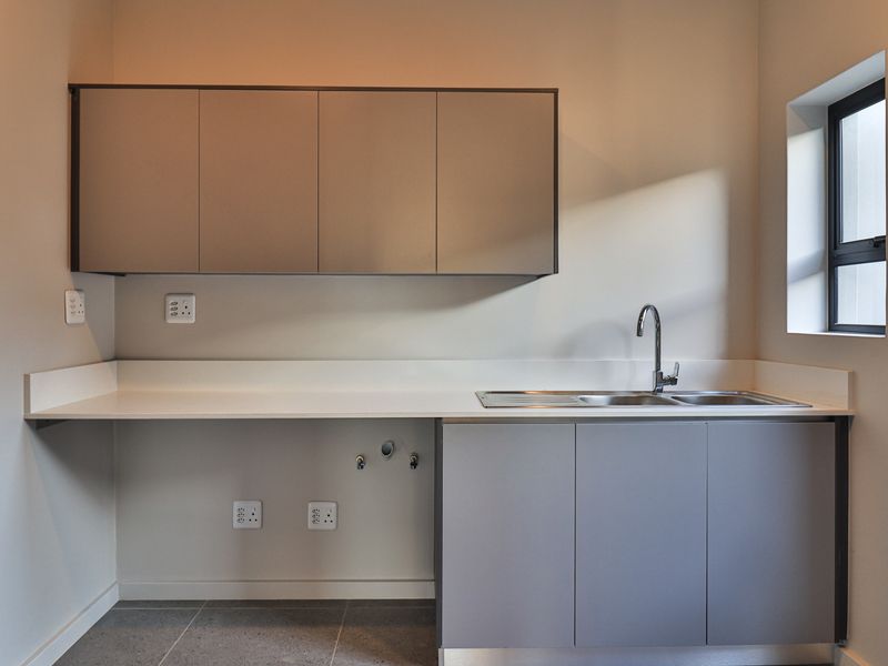 A clean, modern laundry room featuring built-in cabinetry, a stainless steel sink with mixer tap, and stone countertops with dedicated plumbing and electrical points.