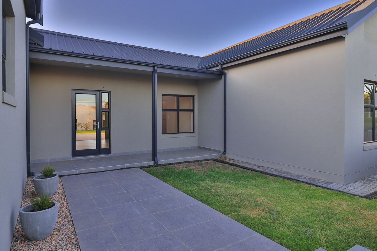 A modern rear exterior view featuring a covered tiled patio, clean rendered walls, dark metal roofing, and contemporary aluminium-framed windows and doors.
