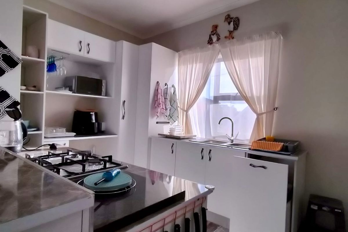 A functional kitchen featuring white cabinetry, stone countertops, a gas hob, and a double sink with a window view.
