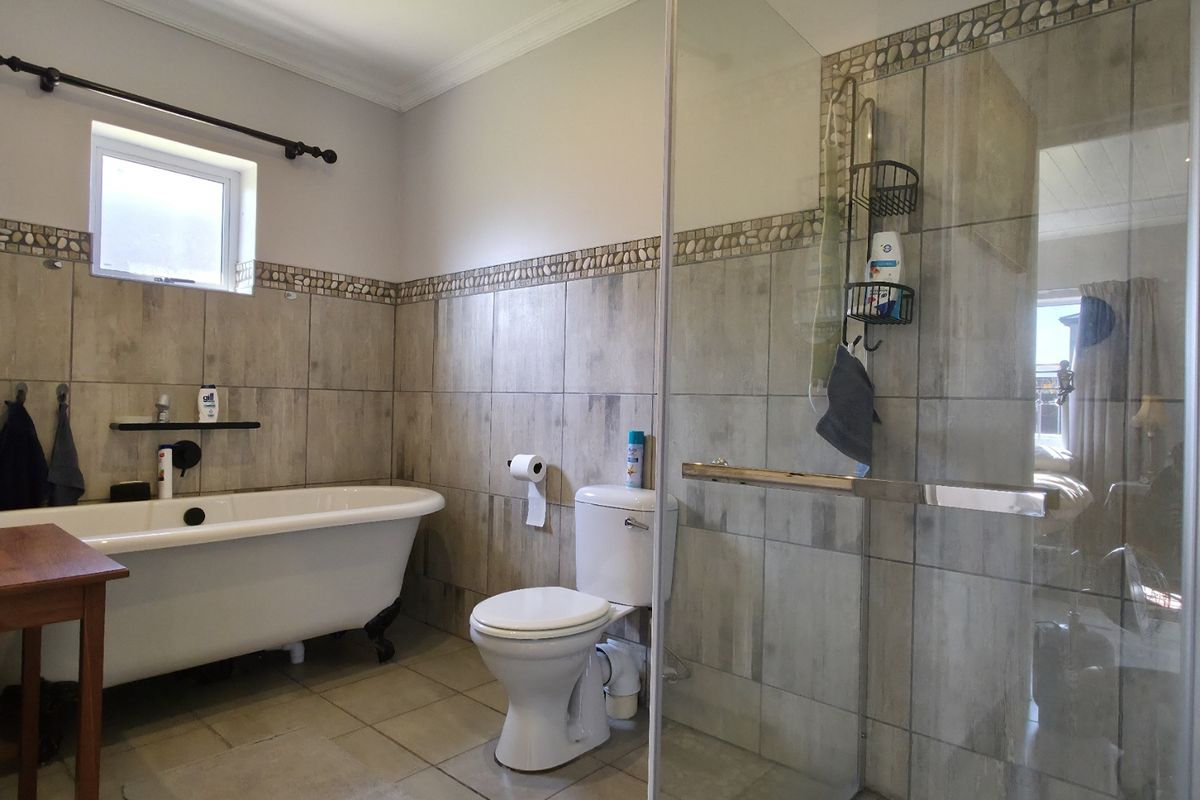 A bathroom featuring a freestanding clawfoot bathtub, a separate glass-enclosed shower, a toilet, and neutral wall tiling with decorative mosaic accents.