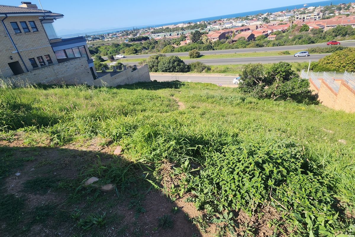 Elevated view overlooking the sloped residential vacant land with surrounding neighborhood and coastal landscape in the distance.