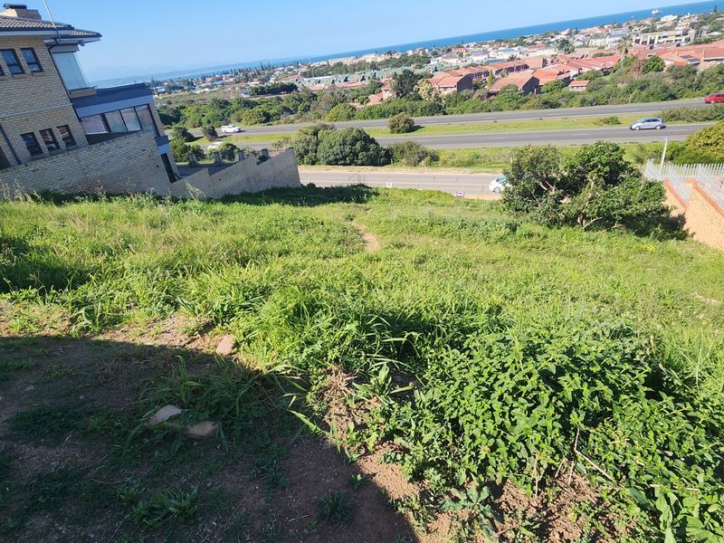 Elevated view overlooking the sloped residential vacant land with surrounding neighborhood and coastal landscape in the distance.