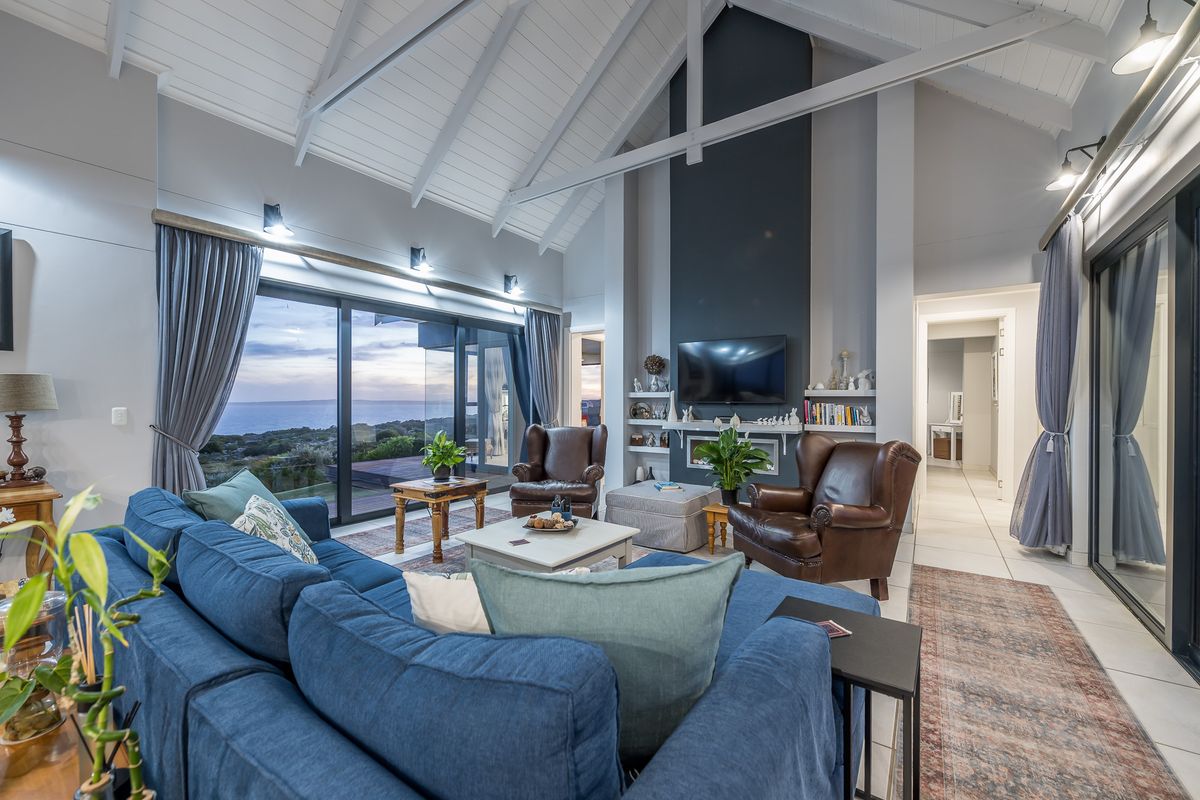 Spacious living room featuring a high vaulted ceiling, exposed beams, a feature fireplace wall, and large sliding glass doors opening to a scenic view.