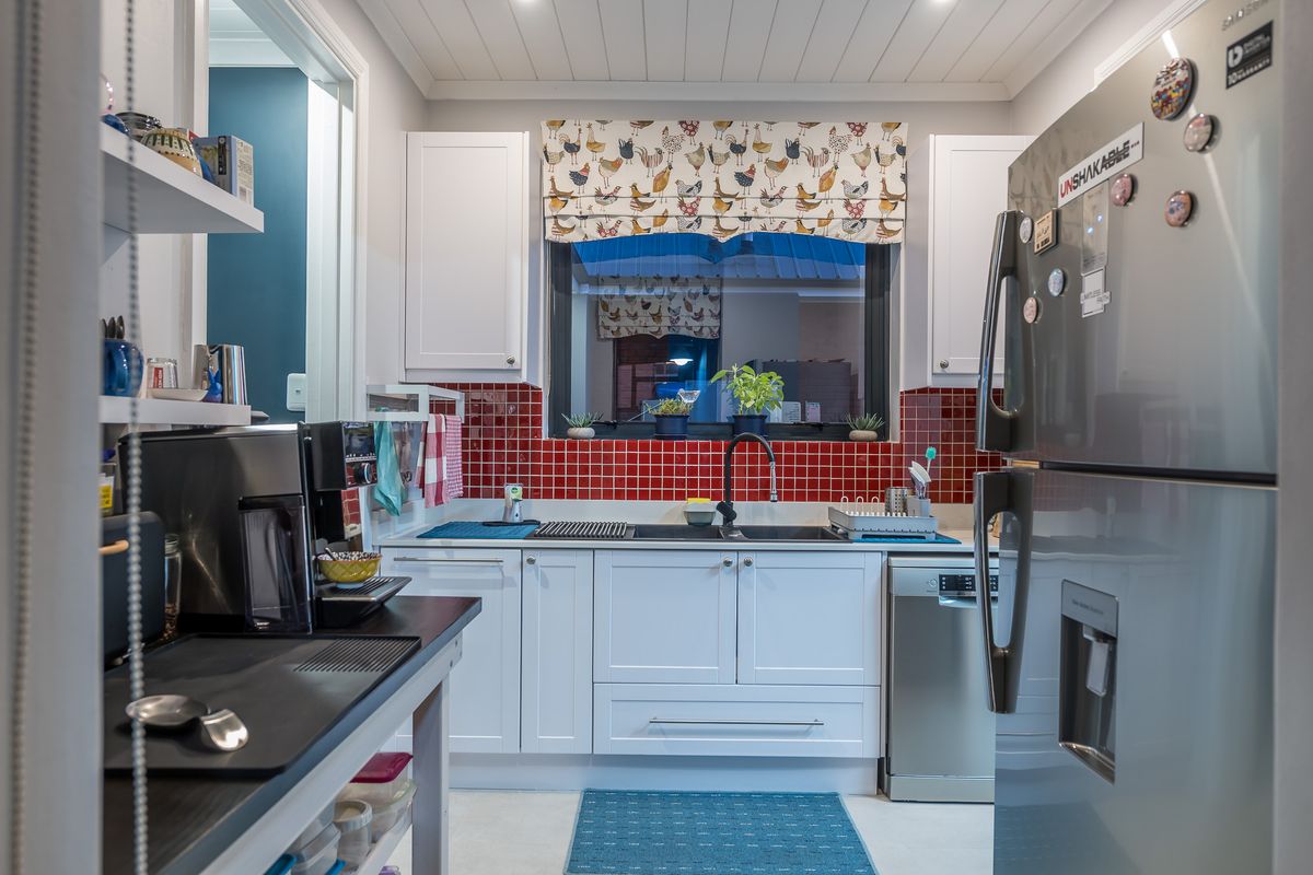 A functional kitchen featuring white cabinetry, a red tiled backsplash, a double sink with a modern faucet, and integrated dishwasher space.