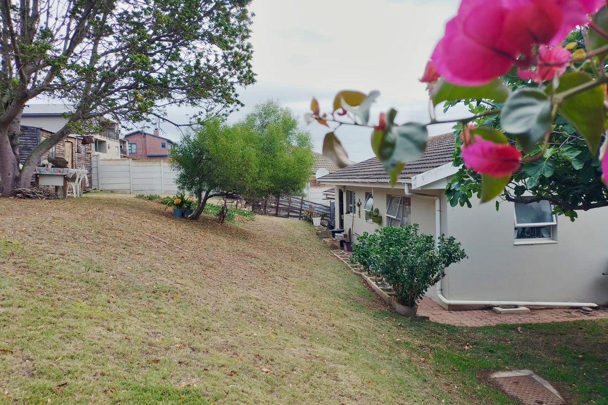 A view of the rear garden featuring a sloped lawn, paved walkway along the house exterior, and precast concrete boundary walling.