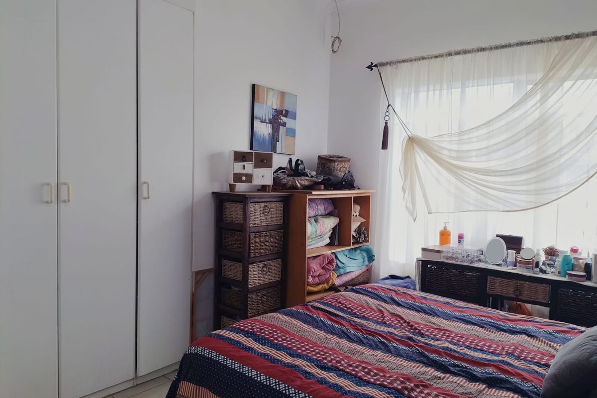 A bedroom featuring built-in wardrobes, tiled flooring, and a window with curtain fixtures. The space requires minor maintenance to address exposed wiring.