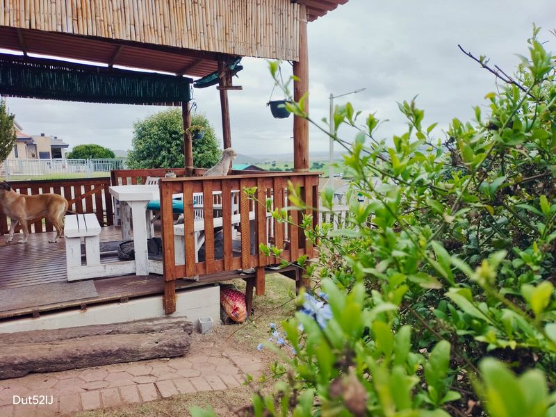 A covered outdoor timber deck patio featuring a rustic timber balustrade and thatched roof structure, overlooking the surrounding landscape.