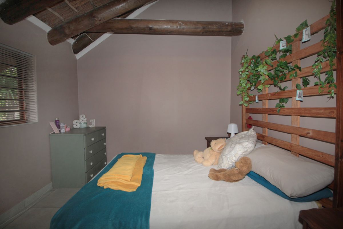 A bedroom featuring exposed timber rafters, tiled flooring, and venetian blinds, offering a cozy atmosphere with potential for modern updates.