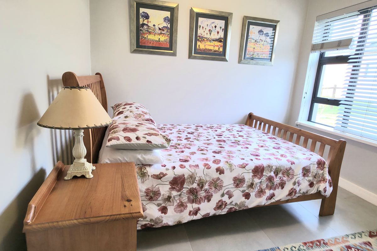 A well-lit bedroom featuring neutral walls, tiled flooring, and a large window with fitted blinds, providing a clean and functional living space.