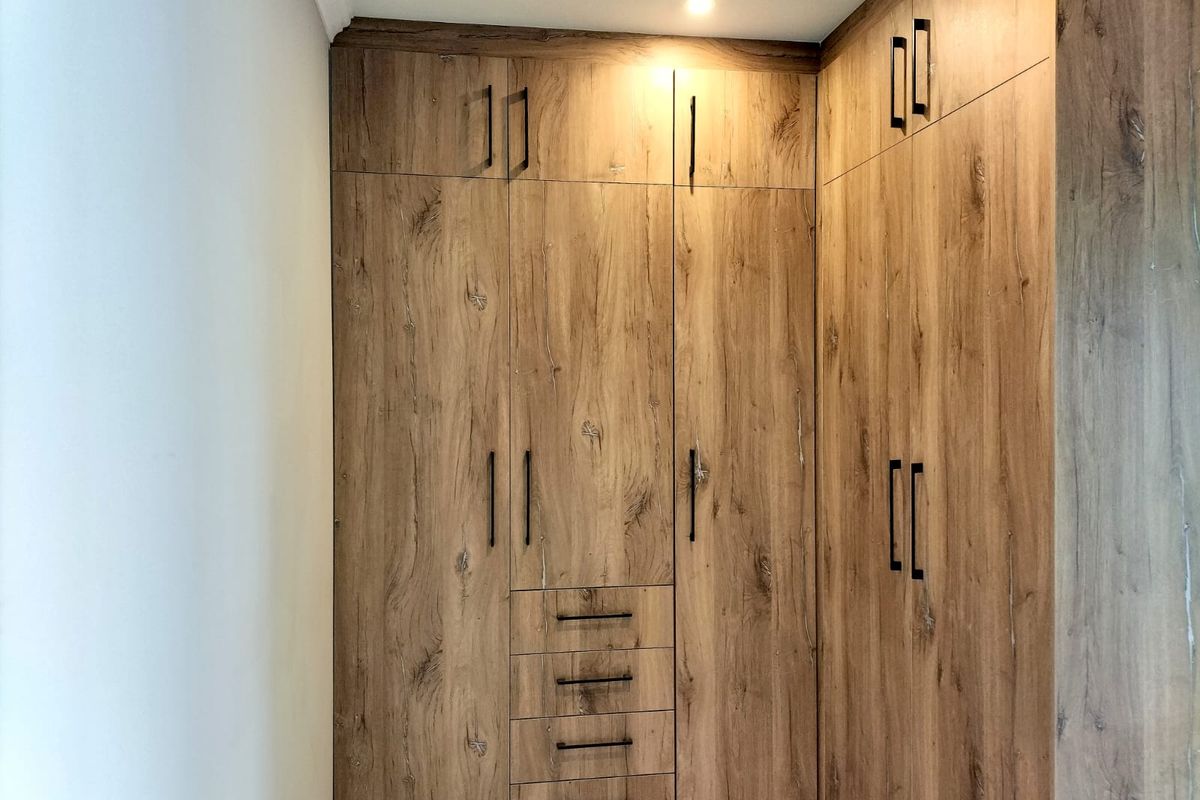 A modern bedroom featuring floor-to-ceiling built-in cupboards with a wood-grain finish and sleek black handles.