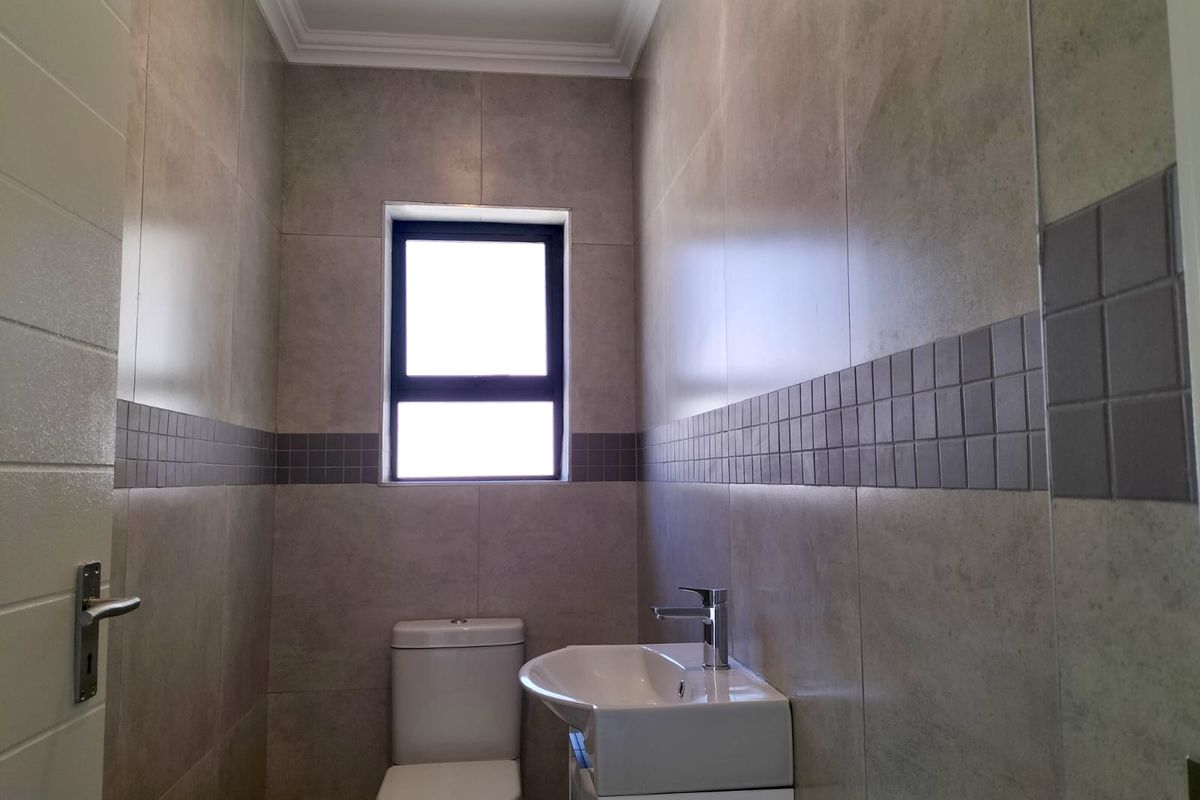 A clean and modern guest bathroom featuring neutral wall tiles, a vanity basin with a mixer tap, and a standard toilet.
